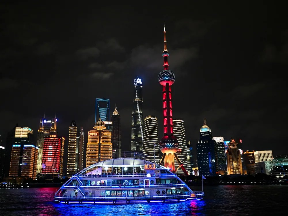 Un barco de crucero perfilado con luz azul en el Huangpu de noche, con la roja Torre de la Perla Oriental y las torres de Pudong al fondo