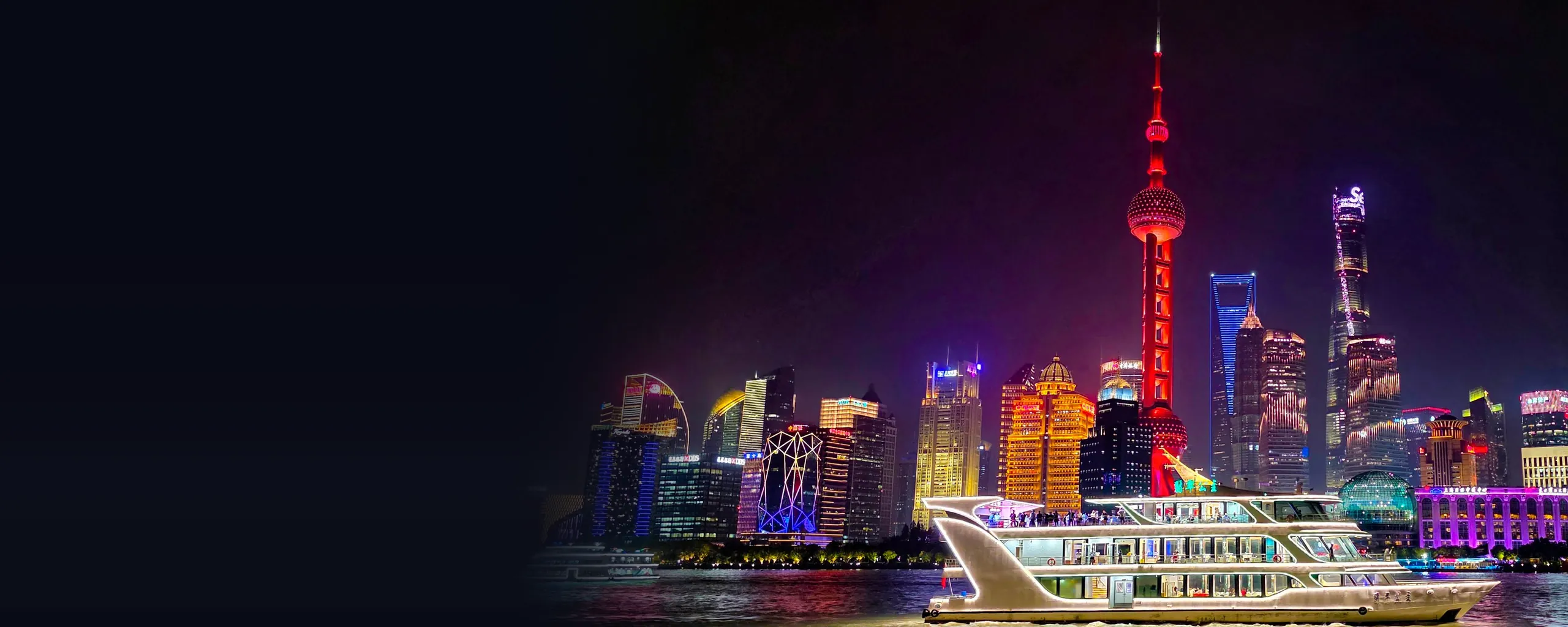 Un barco de crucero iluminado en el río Huangpu de noche, con la roja Torre de la Perla Oriental y las resplandecientes torres de Pudong alzándose tras él