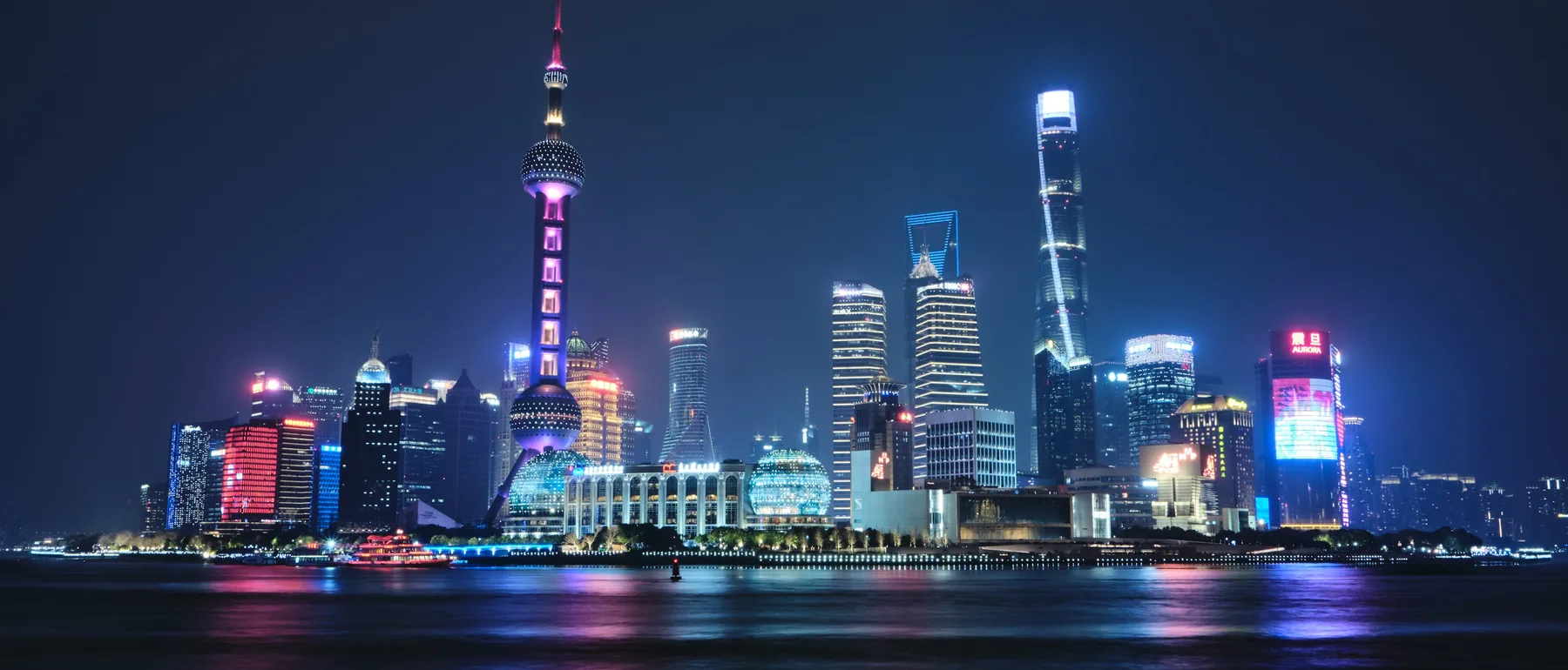El horizonte de Pudong al otro lado del Huangpu de noche, con la Torre de la Perla Oriental y las torres de cristal reflejadas en el agua